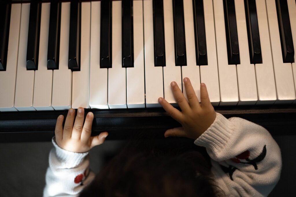 子どもの手がピアノの鍵盤を触っている